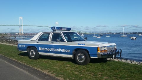 1991 Ford LTD Crown Victoria - Metropolitan Police Crown Victoria parked by the water with a bridge and sailboats in the distance.