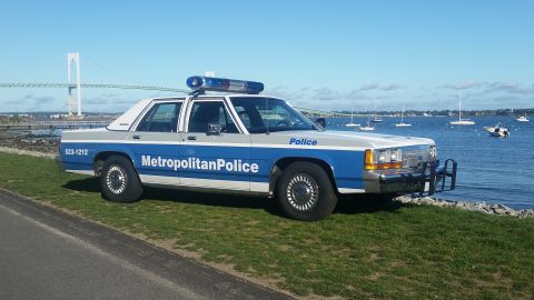 1991 Ford LTD Crown Victoria - A 1991 Ford Crown Victoria police car is parked near the water with boats and a bridge visible.