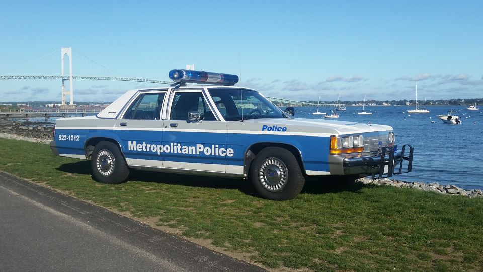 Police car parked by the water with a bridge in the background