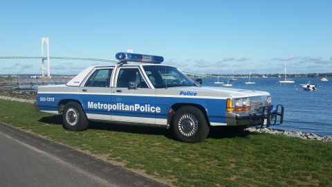 1991 Ford LTD Crown Victoria - A 1991 Ford Crown Victoria police car is parked near the water, with a bridge and sailboats visible.
