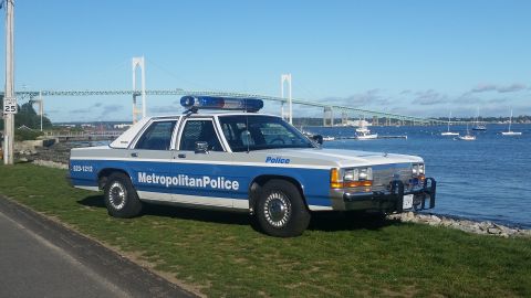1991 Ford LTD Crown Victoria - Police car parked by the water with a bridge in the distance.