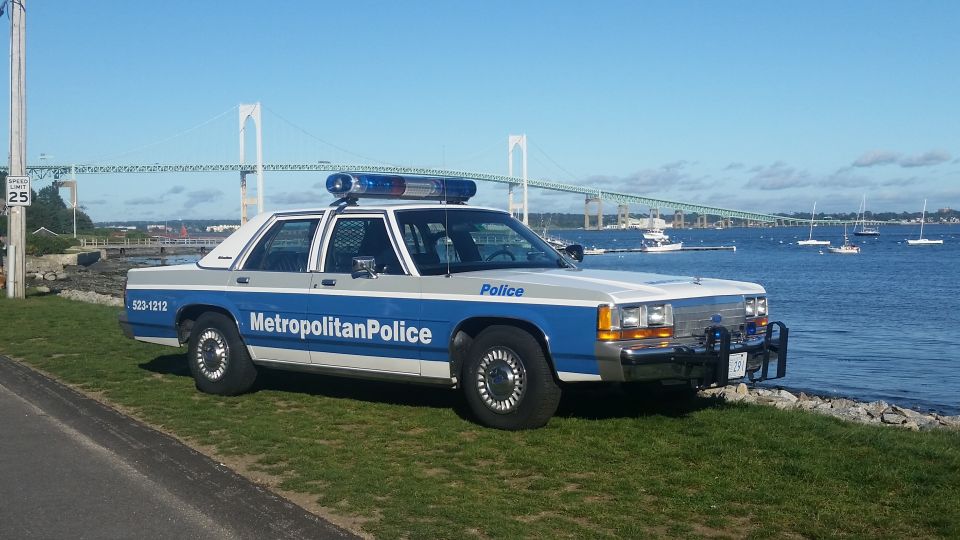 1991 Ford Crown Victoria police car parked on grass near water, bridge in background. "Metropolitan Police" text on door
