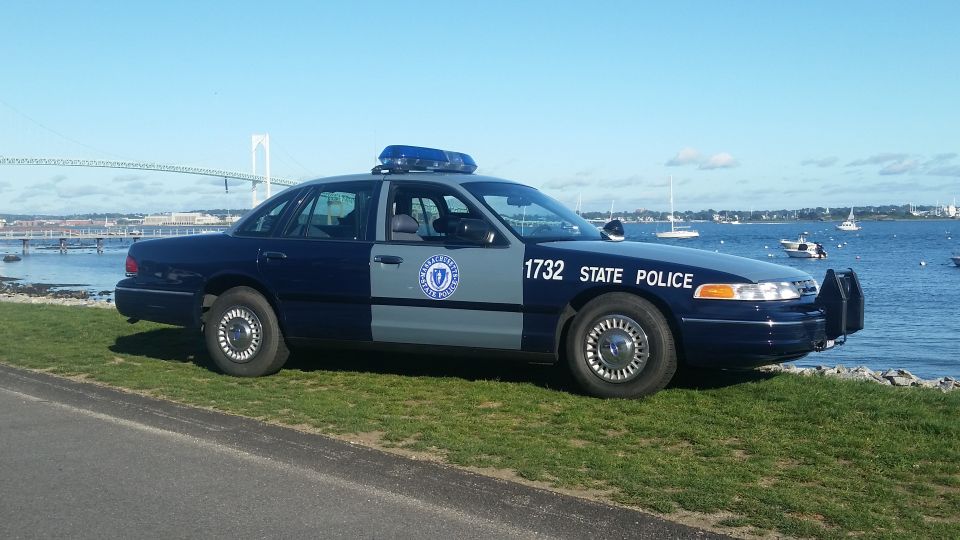 Side view of a 1991 Ford Crown Victoria police car parked by the water with a bridge in the background
