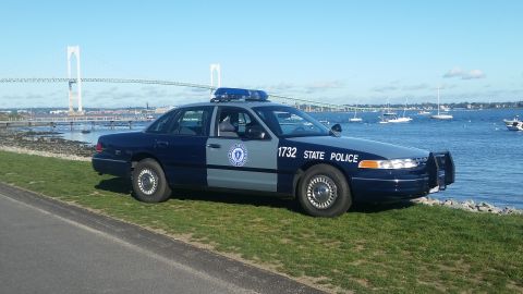 1991 Ford LTD Crown Victoria - A 1991 Ford Crown Victoria police car is parked near the water, with a bridge and sailboats visible in the distance.