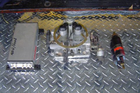 1974 Ford Bronco - Automotive parts including a carburetor, fuel injector, and electronic control module are laid out on a diamond plate surface.