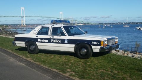 1991 Ford LTD Crown Victoria - A 1991 Ford Crown Victoria police car is parked by the water with a bridge in the background.