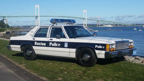 1991 Ford LTD Crown Victoria - A Boston Police car is parked near the water, with a large bridge visible in the distance.