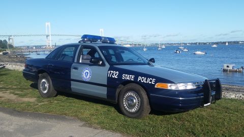 1991 Ford LTD Crown Victoria - A 1991 Ford Crown Victoria police car is parked near the water, with a bridge and boats visible in the distance.