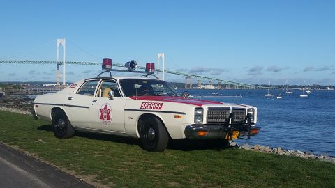 1991 Ford LTD Crown Victoria - This vintage police car, likely from the late 1970s, is parked near the water with a bridge visible in the distance.