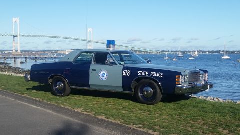 1991 Ford LTD Crown Victoria - A two-tone blue and grey state police car is parked near the water, with a large bridge visible in the distance.