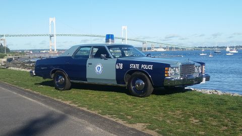 1991 Ford LTD Crown Victoria - A vintage police car with "STATE POLICE" text and a blue light bar sits by the water under a clear sky.