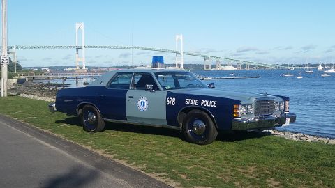 1991 Ford LTD Crown Victoria - A two-tone blue and gray police car is parked by the water with a bridge in the background.