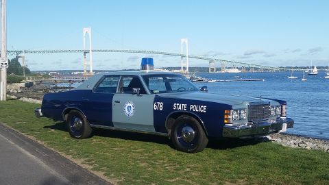 1991 Ford LTD Crown Victoria - A vintage police car with 'STATE POLICE' text and number 678 is parked by the water with a bridge in the background.