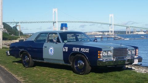 1991 Ford LTD Crown Victoria - A vintage police car, marked "STATE POLICE" and numbered 678, sits by the water with a large bridge in the distance.