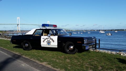 1991 Ford LTD Crown Victoria - This highway patrol car is parked near the water, with a bridge and several boats visible in the distance under a clear blue sky.