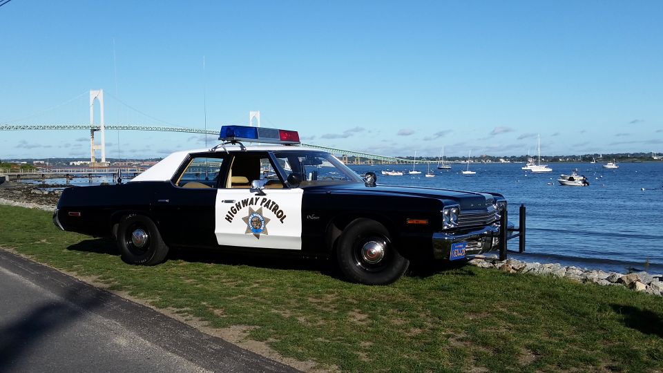 Black and white highway patrol car parked by the water with a bridge in the background