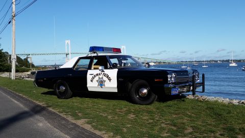 1991 Ford LTD Crown Victoria - A 1977 Ford LTD patrol car, marked "Highway Patrol", sits parked by the water with a bridge in the background.
