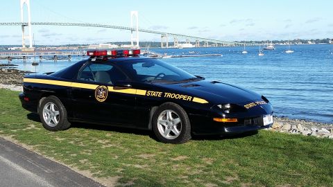 1991 Ford LTD Crown Victoria - State Trooper car parked near the water, with a bridge visible in the distance.