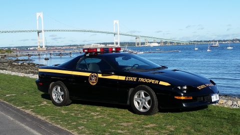1991 Ford LTD Crown Victoria - A black state trooper car is parked on a grassy area next to the water, with a large bridge visible in the distance.