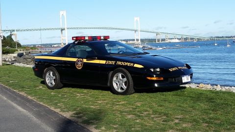 1991 Ford LTD Crown Victoria - A black 1997 Chevrolet Camaro Z28 police car is parked near the water with a bridge in the distance.