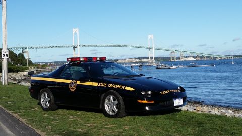 1991 Ford LTD Crown Victoria - A black police car with "STATE TROOPER" markings is parked by the water, with a large bridge visible in the distance.