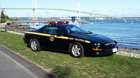 1991 Ford LTD Crown Victoria - State trooper car parked near the water, with a bridge and boats visible in the background.