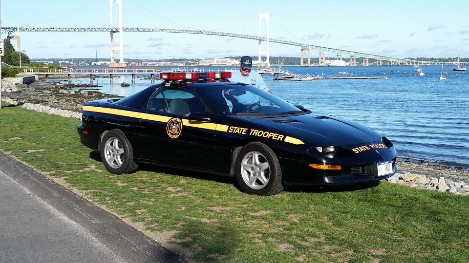 Black state trooper car with yellow stripe and "STATE TROOPER" text, parked by the water with a bridge in the background. This appears to be a 1995 Chevrolet Camaro