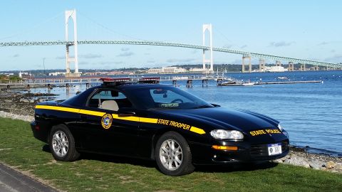 1991 Ford LTD Crown Victoria - A black state trooper car is parked on a grassy area near the water, with a large bridge visible in the distance.