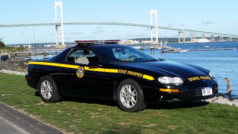 1991 Ford LTD Crown Victoria - State trooper car parked near a body of water with a large bridge in the distance.