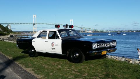 1991 Ford LTD Crown Victoria - A vintage police car with a two-tone paint scheme sits by the water, a bridge visible in the distance.