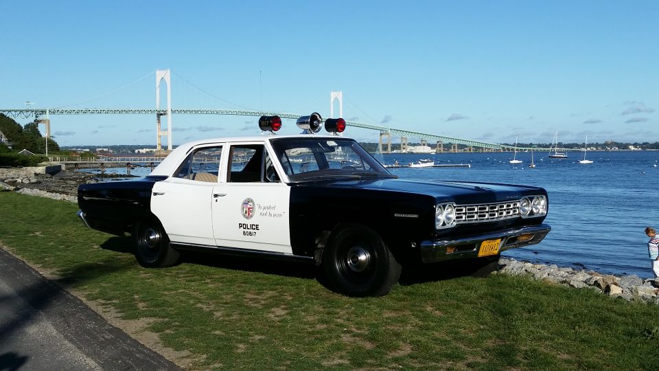 Black and white police car parked by the water with a bridge in the background