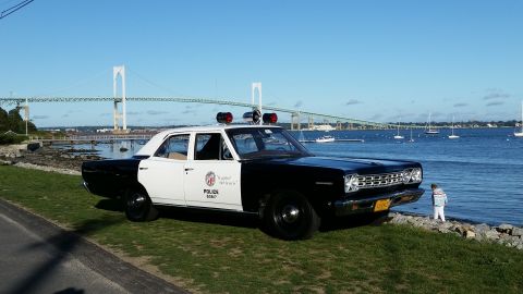1991 Ford LTD Crown Victoria - A vintage police car with a two-tone paint scheme sits by the water under a clear blue sky.