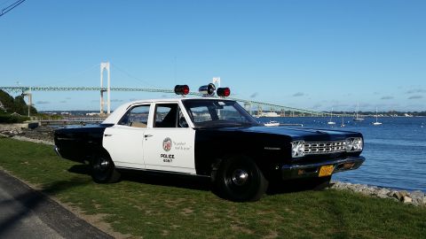 1991 Ford LTD Crown Victoria - This vintage police car, likely a 1968 model, is parked near the water with a large bridge visible in the distance.