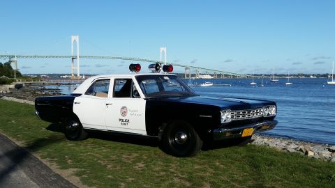 1991 Ford LTD Crown Victoria - Vintage police car with light bar and siren sits by the water with a bridge in the distance.