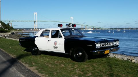 1991 Ford LTD Crown Victoria - This police car is parked near the water with a bridge and boats in the distance.