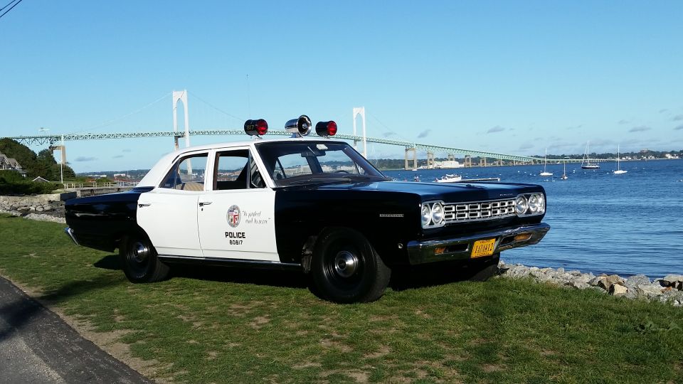 Black and white police car parked on grass by the water, with a bridge in the background