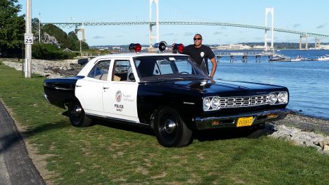 1991 Ford LTD Crown Victoria - A man poses with a vintage police car, a two-tone paint scheme and emergency lights, near a bridge and waterfront.