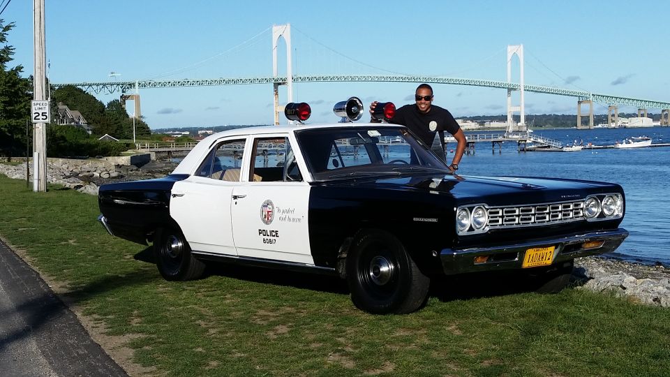 Black and white police car, 1968 model, with a man standing by the driver's side door. Police markings are visible on the door