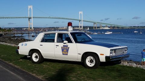 1991 Ford LTD Crown Victoria - A vintage police car is parked near the water, with a large bridge spanning the bay in the distance.
