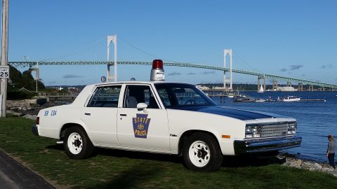 1991 Ford LTD Crown Victoria - This 1978 Chevrolet Malibu police car, marked "STATE POLICE", is parked near the water with a large bridge in the background.