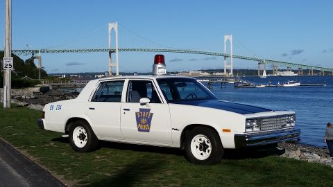 1991 Ford LTD Crown Victoria - This 1980s police car is parked near the water with a large bridge in the distance.