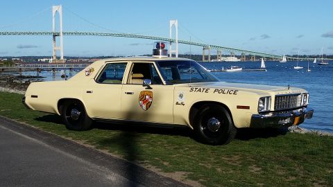 1991 Ford LTD Crown Victoria - This 1977 Plymouth Gran Fury police car is parked by the water with a bridge in the background.