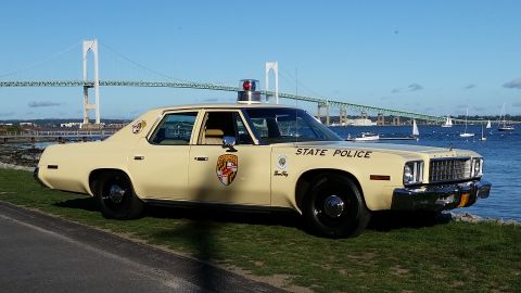 1991 Ford LTD Crown Victoria - A vintage state police car is parked near the water, with a large bridge spanning the bay in the distance.