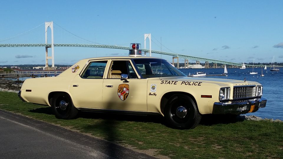 cream colored police car with 'STATE POLICE' on the door, parked by the water with a bridge in the background