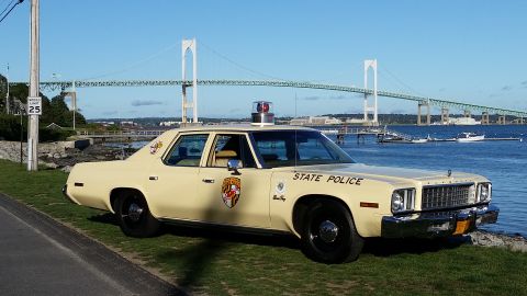 1991 Ford LTD Crown Victoria - A vintage cream-colored police car, marked "STATE POLICE" with a Maryland emblem, sits parked by the water with a large bridge in the dista…