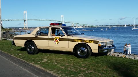 1991 Ford LTD Crown Victoria - A vintage state police car is parked near the water with a bridge in the distance.