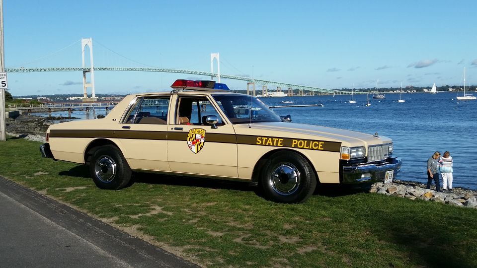 tan state police car parked by water, bridge in background