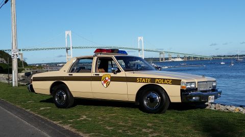 1991 Ford LTD Crown Victoria - A vintage Maryland State Police car is parked by the water with a large bridge in the distance.