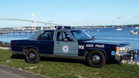 1991 Ford LTD Crown Victoria - A 1991 Ford Crown Victoria police car is parked by the water, with a bridge and sailboats visible in the distance.