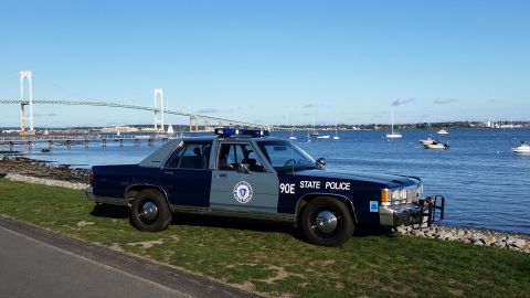 1991 Ford LTD Crown Victoria - A 1991 Ford Crown Victoria police car is parked near the water with boats and a bridge in the distance.